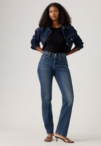 Høyt liv denimjeans med rett ben, med en klassisk denimtekstur. Kombinert med en tettsittende svart topp og denimjakke.