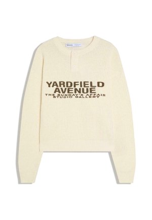 Kremowy sweter z dzianiny z długim rękawem, z kołnierzem henley zapinanym na trzy guziki oraz brązowym napisem na przodzie: "YARDFIELD AVENUE THE SUNDAY'S AFFAIR STUDIO GALLERY".