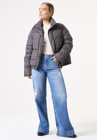 Doudoune matelassée gris foncé avec un col haut, associée à un jean large dégradé bleu clair et des chaussures noires.