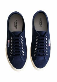 Sneakers in tela blu con un classico design a lacci, suole in gomma bianca e occhielli in argento, accompagnati da un piccolo etichetta rossa e bianca.