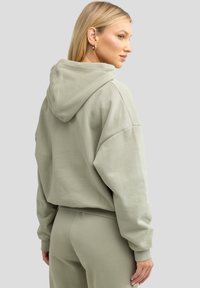 Hellgrüner Hoodie mit einer lockeren Passform, großer Kapuze und gerippten Bündchen. Das Material wirkt weich und strukturiert und wird stilvoll mit passenden Hosen kombiniert.
