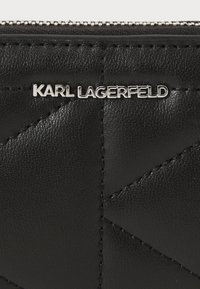 Black leather wallet with a quilted pattern and silver "Karl Lagerfeld" logo. Features a zipper closure and fine stitching details.