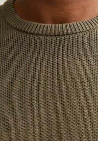 Maglione lavorato a maglia verde oliva con una trama testurizzata, caratterizzato da un collo rotondo a coste. Il tessuto ha un aspetto morbido e leggermente oversize.