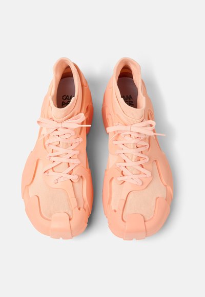 Peach-colored athletic shoes with a textured mesh upper, chunky sole, and intricate, molded rubber accents. Features decorative lace system.