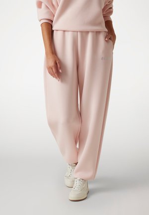 Pantalons de survêtement roses clairs en tissu doux, avec une coupe ample et des poches latérales, associés à des baskets montantes blanches.