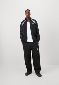 Black athletic jacket with gray accents, paired with black pants. Made of lightweight material, featuring a zip front and logo details.