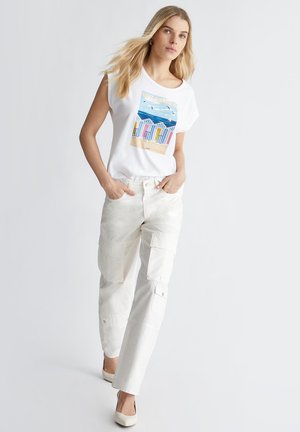 T-shirt bianco a maniche corte con una grafica colorata di una scena seaside. Abbinato a pantaloni beige cargo con molteplici tasche.