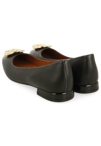 Bailarinas de cuero negro con tacón bajo, punta redondeada y adornos decorativos dorados en la parte superior. Textura suave con un acabado mate.