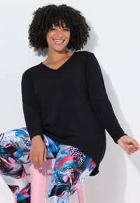 Schwarzes Langarmoberteil mit V-Ausschnitt, kombiniert mit lebhaften, gemusterten Leggings, die florale und abstrakte Designs in Blau, Pink und Schwarz aufweisen.