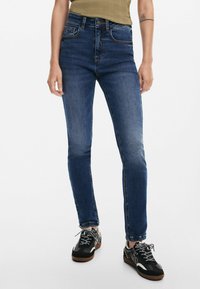 Slim-fit, mörkblå denimjeans med en urtvättad finish, fem fickor och subtila sömnadsdetaljer, i kombination med svarta sneakers.