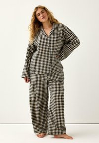 Czarny i beżowy zestaw piżamowy w kratę, składający się z koszuli z kołnierzykiem zapinanej na guziki oraz spodni z szerokimi nogawkami. Materiał wydaje się być miękki, a krój jest luźny.