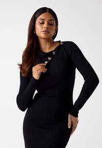 Czarna dzianinowa sukienka z prążkowanym wzorem, z długimi rękawami, dopasowanym krojem i złotymi akcentami na ramieniu.
