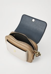 Compact crossbody bag in beige and cream leather with a navy interior, zip closure, and gold hardware accents. Features a front pocket.