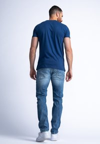 Granatowa koszulka z krótkim rękawem, zestawiona z jasnoniebieskimi dżinsami oraz białymi trampkami. Prosty design z gładką fakturą.