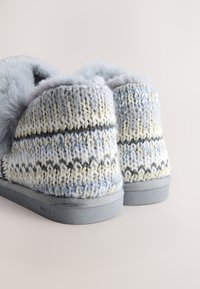 Chaussons en tricot bleu clair avec un motif texturé, des accents gris et crème, une doublure douce et des semelles en caoutchouc gris.