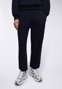 Granatowe dresy wykonane z miękkiego materiału, z elastycznym pasem i prostym krojem, zestawione z metalicznie srebrnymi butami sportowymi.