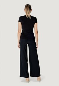 T-shirt aderente nera abbinato a pantaloni neri a vita alta e a gamba larga, realizzati in tessuto morbido. I capelli del modello sono raccolti in una coda di cavallo.