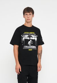 Sort bomulds t-shirt med grafisk tryk af Isaac Hayes og gul tekst. Korte ærmer og en afslappet pasform, parret med sorte cargo-bukser.