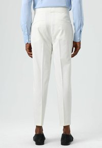 White tailored trousers with a slim fit, featuring pressed pleats, belt loops, and back pockets. Paired with a light blue shirt and black shoes.