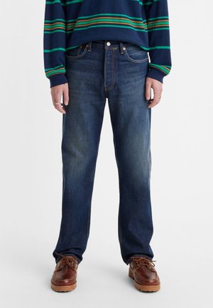 Dark blue straight-leg jeans with faded front, five-pocket design, and contrasting stitching. Paired with a striped navy sweater.