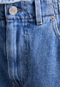 Denim tkanina u svijetloplavoj boji s vidljivom teksturom; sadrži pojas s srebrnim gumbom i kontrastnim narančastim šavovima uz detalje šavova.