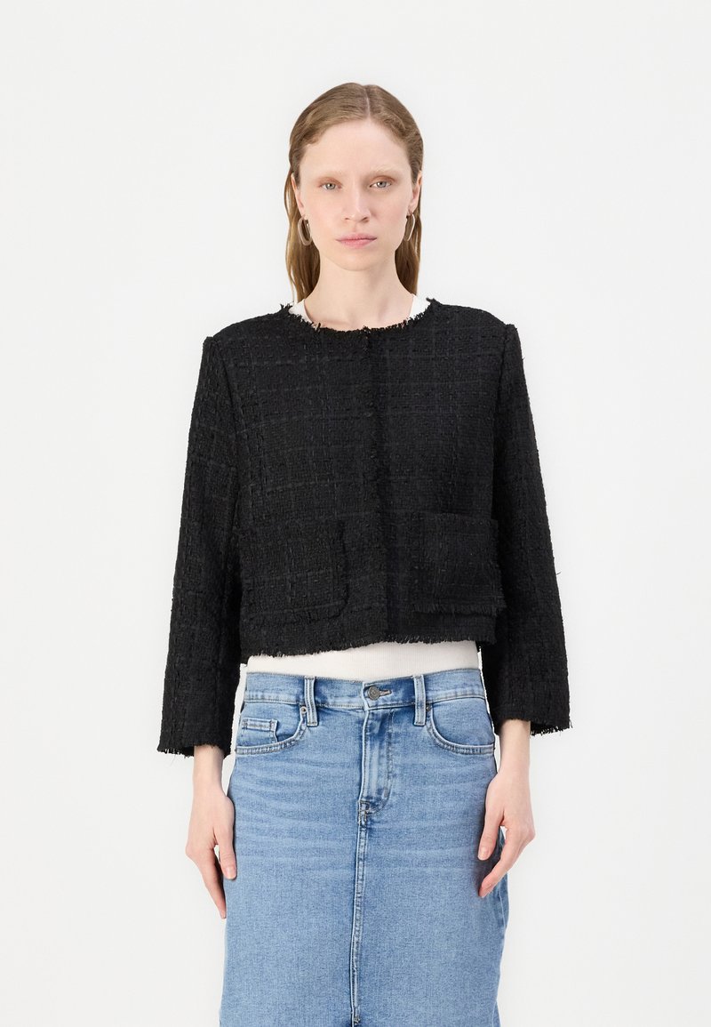 Svart tweed, kort jakke med teksturert overflate, rund hals og to frontlommer, sammen med en hvit topp og blå denimskjørt.