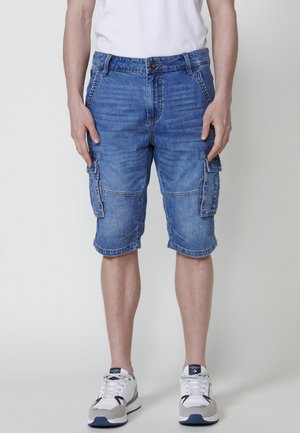 Lichtblauwe denim cargo shorts met meerdere zakken, een knoopsluiting en omgeslagen zomen. Gecombineerd met witte sneakers.