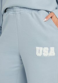 Ljusblå mjukisbyxor med elastisk midja och en vit frotté-logotyp "USA" broderad på vänster lår.