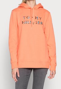 Koralli värinen huppari, jossa on elastiset hihansuut ja helma. Hupparissa on "TOMMY HILFIGER" -teksti monivärisessä painatuksessa etupuolella.