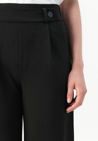 Černé tailored kalhoty vyrobené z hladké tkaniny, s širokým pasem, jedním knoflíkem na zapínání a předními sklady pro strukturovaný střih.