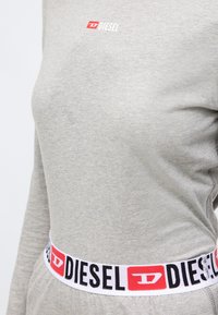 Sivi pamučni dukserica dugih rukava s malim bijelim logotipom "DIESEL". Bijeli pojas sa crnim i crvenim oznakama "DIESEL". Glatka tekstura.