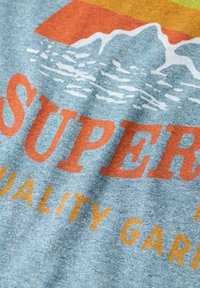 Una tela de color azul jaspeado presenta un texto en negrita en naranja y amarillo que dice "SUPER" y "PRRROPUESTA DE CALIDAD" junto a un gráfico de montañas y una ilustración de agua.