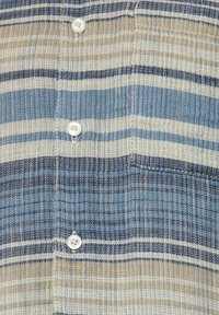 Camisa de botones con un tejido texturizado y rayas horizontales en beige, azul claro y azul oscuro. Incluye cierre con dos botones blancos.