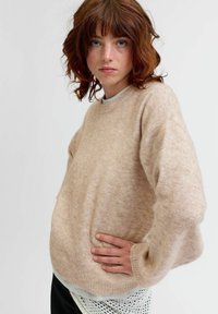 Beżowy sweter z wełny o okrągłym dekolcie, obniżonych ramionach i długich rękawach, wyróżniający się miękkim, teksturowanym materiałem i luźnym krojem.