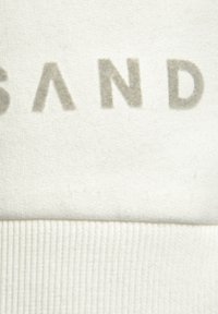 White sweatshirt fabric with a textured finish. The design features the letters "SAND" in a light grey, slightly raised print.