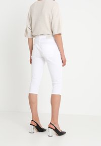 Pantalones capri blancos combinados con una blusa de punto suelta en color beige y zapatos slingback negros con tacones cuadrados plateados. Diseño sencillo con un ajuste casual.