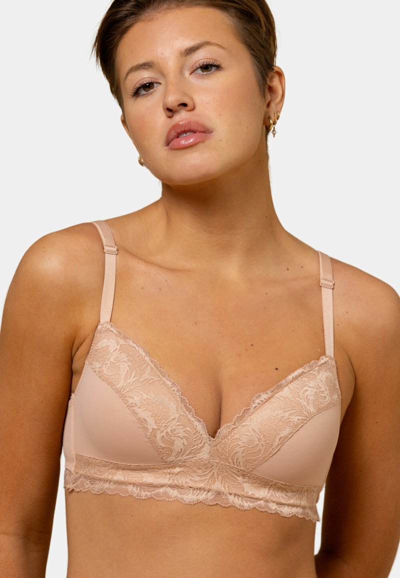 Soutien-gorge rose clair en tissu lisse avec des accents en dentelle sur les bonnets et la bande. Il dispose de bretelles réglables et d'un design en V.