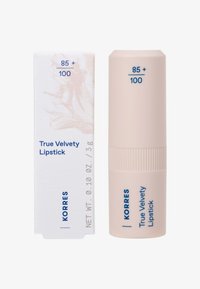 Le rouge à lèvres True Velvety de Korres dans un tube rose pâle avec une texture striée, accompagné d'une boîte blanche ornée d'un design abstrait doux et de texte bleu.