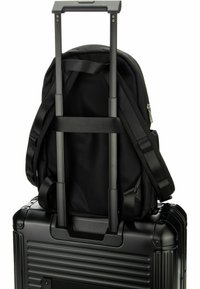Mochila negra con correas ajustables reposando sobre una maleta rígida negra con un mango telescópico y un cuerpo texturizado.