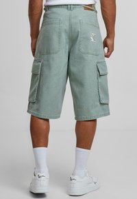 Shorts cargo en denim vert clair, avec deux poches latérales, deux poches au dos et une surface texturée avec une étiquette sur la ceinture.