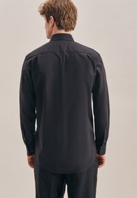 Zwarte langwerpige shirt met een standaard kraag, knoopmanchetten en een gladde textuur, ontworpen met een moderne, getailleerde silhouet.