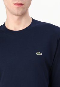 Sweatshirt en coton marine avec un col rond et un petit logo crocodile vert brodé sur la poitrine. Texture douce, design décontracté.