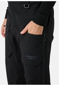 Zwarte outdoorbroek met ritszakken en een logo. Gemaakt van duurzame stof en met een getailleerd ontwerp. Duidelijke stikseldetails.