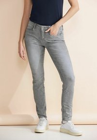 Harmaa farkkuhousut slim fit -mallilla, viisi(tasku)suunnittelulla ja nappisuljennalla, yhdistettynä valkoisiin tennareihin. Sujuva pinta ja kapenevat lahkeet.