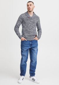 Strikket sweater i blågrå blanding, med sjalskrave og knapdetalje. Kombineret med klassiske blå jeans og hvide sneakers.