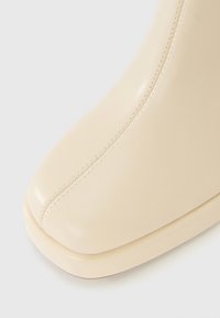 Beige lærboot med firkantet tå og synlig syning som løper vertikalt nedover midten foran.