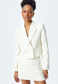 Weißer strukturierter Blazer mit doppelten Knöpfen, kombiniert mit einem passenden, taillierten Rock. Beide Teile weisen ein Strickmuster und einen cropped Schnitt auf.