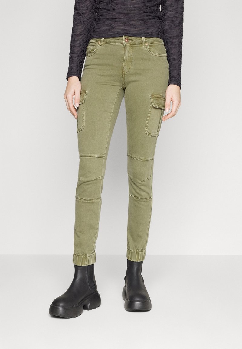 Vihreät laivastohousut slim-fit-leikkauksella, joissa on sivutaskut ja joustavat hihnat, yhdistettyinä mustiin nilkkabootseihin. Pehmeä kankaan pinta.