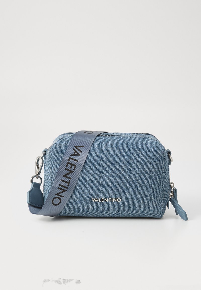 Blue denim crossbody bag with a rectangular shape, silver hardware, and a logo-embossed fabric strap. Smooth texture and zipper closure.