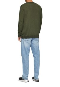 Olijfgroen gebreid sweater met geribde mouwen en onderrand, gedragen met lichtblauwe loszittende denim jeans en zwarte schoenen.